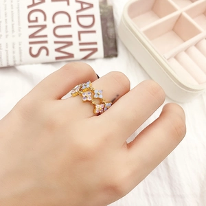 Close-up of golden floral ring with iridescent opal petals worn on a hand over jewelry box