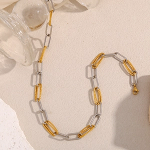 Detail of mixed silver and 18K gold plated paperclip twist chain necklace on beige surface