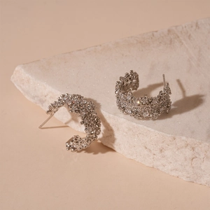 Macro shot of silver C-shaped earrings with micro-pave zircons on stone background