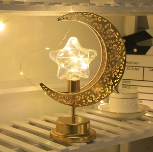 Vista detallada de una lámpara de mesa decorativa LED dorada con luna y estrella con luz cálida.