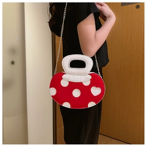 Red and white polka dot heart crossbody bag with metal chain strap worn by a model