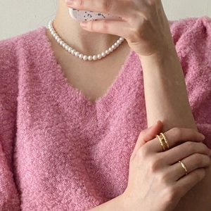 Close-up of dual-layer golden H-shape open ring and pearl necklace on a soft knit sweater
