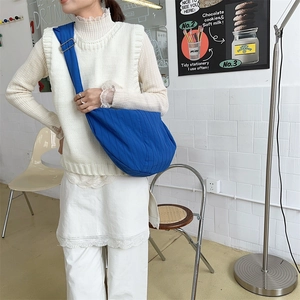 Detail of dark blue dumpling bag with pleated texture worn by model in casual style