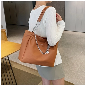 Brown leather tote bag with silver chain worn by a model in a modern office setting