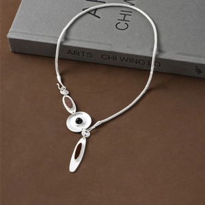 Minimalist matte silver irregular disc necklace with enamel inlays on a grey book base