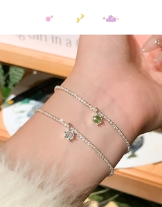 Detailed shot of two silver star bracelets with emerald and white zircon charms on wrist