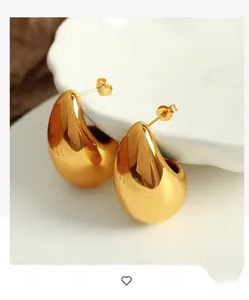 Close-up of golden teardrop earrings with a mirror-polished finish on a white porcelain dish