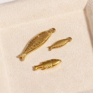 Three golden fish-shaped stainless steel pendants with detailed scales on white velvet