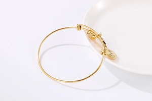 Detail of adjustable gold wire bracelet with circular charm on white ceramic display