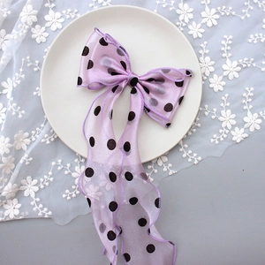 Pink sheer bow hair clip with black polka dots and long ribbons on a lace background