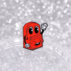 Cute red cartoon backpack enamel pin badge displayed on textured glass with bokeh background