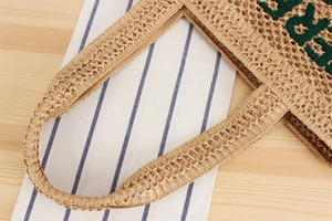 Gros plan détaillé d'un sac en paille tissé à la main avec lettres brodées vertes