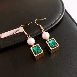 Close-up of gold earrings with green square gemstones and elegant white pearls on leather