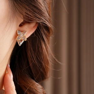 Close-up of elegant gold four-leaf clover stud earrings with sparkling zircon on a model