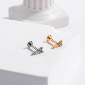 Detailed view of silver and gold arrow labret studs with zircon on white stone