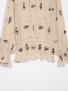 Detail of beige sheer shirt featuring sequin embroidery, elastic waist and ruffle cuffs
