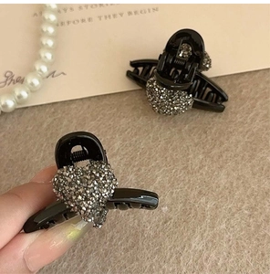 Close-up of a small black heart-shaped hair claw clip with shiny grey rhinestones