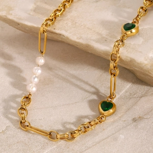Close-up of gold chain necklace with white pearls and green heart charms on stone