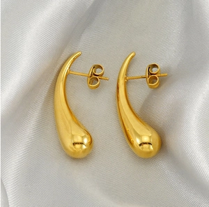 Detailed view of glossy gold teardrop earrings on elegant silver silk fabric