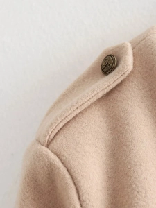 Detailed macro view of the beige wool jacket shoulder featuring a vintage crest metal button