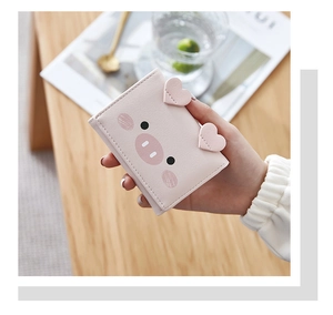 Detailed view of a cute pink pig-shaped small leather wallet held over a wooden table