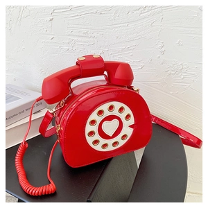 Macro shot of red patent leather crossbody bag in a vintage telephone design with dial
