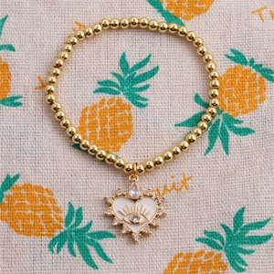 Gold-plated beaded elastic bracelet featuring a white enamel heart with Evil Eye charm