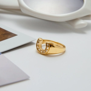 Detail of gold horseshoe ring with white zircons on a white minimalist background