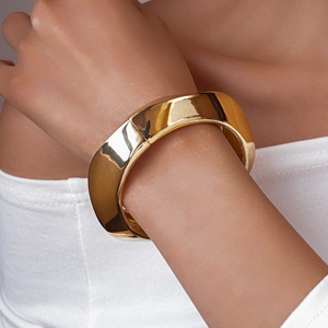 Close-up of a wide polished gold metal cuff bracelet worn on a wrist for a luxury look