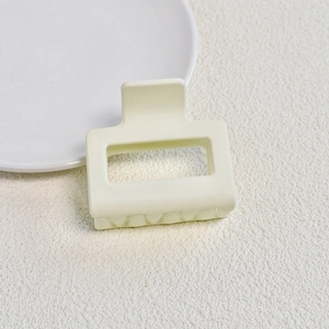 Detail view of a square matte cream hair claw clip with cutout design on textured surface
