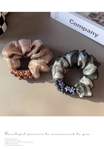 Close-up of mesh scrunchies with delicate flower beads on a beige textured background