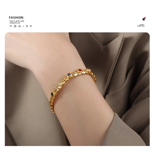 Detailed close-up of a gold-plated bracelet with colorful inlaid gemstones on a wrist