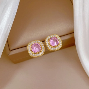 Close-up of golden square earrings with pink center stone on beige jewelry box display