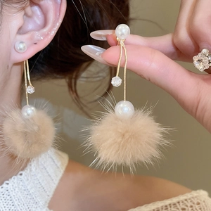 Detail of elegant gold-plated drop earrings with white pearls and soft pompon accents