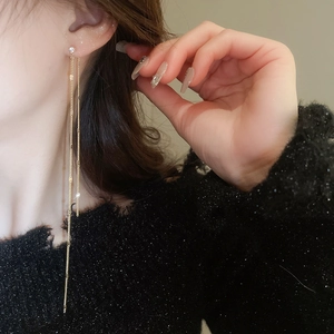 Close-up of long gold tassel earrings with zircon studs worn by a female model