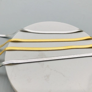 Detail of flat snake bone chain necklaces in gold and silver finish on marble display