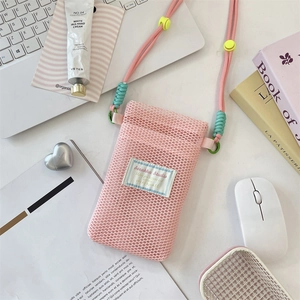 Detail of pink mesh phone bag with adjustable woven strap and brand label on desk