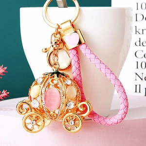 Detailed shot of golden pumpkin carriage keychain with pink gems and braided leather strap