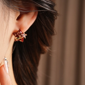 Detailed close-up of a gold-plated star earring with red enamel and angel motif on ear
