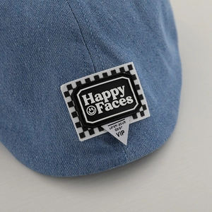 Dettaglio del berretto in denim blu per bambini con toppa Happy Face e motivo a scacchi