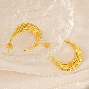 Detailed close-up of textured golden hoop earrings resting on glass tray and glitter fabric