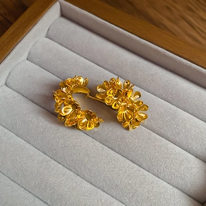 Macro view of gold flower cluster C-shaped earrings on a grey velvet jewelry tray