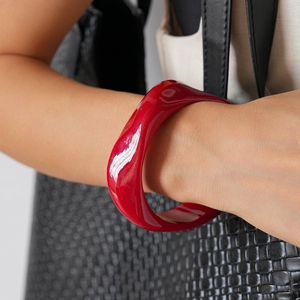 Detail of red irregular geometric acrylic bangle with smooth glossy wave texture