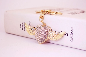 Close-up of golden heart with wings keychain encrusted with crystal rhinestones on a book