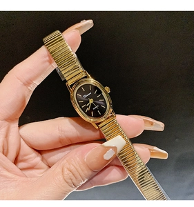 Close-up of a vintage oval gold watch with a black dial and elastic metal strap