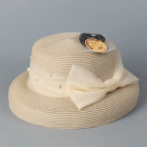 Detail of beige straw sun hat with sheer ribbon, pearls and elegant bow decoration