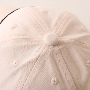 Detail of a beige cotton kids' baseball cap showing a six-panel crown with embroidered eyelets