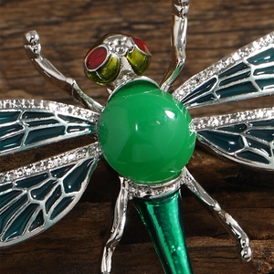 Macro shot of silver dragonfly brooch with green gemstone and enamel wing details