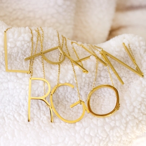 Close-up of 18K gold plated capital letter pendants on a soft white plush surface