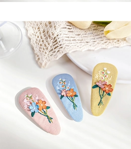 Detail of three embroidered fabric floral hair clips in pink, blue, and yellow colors